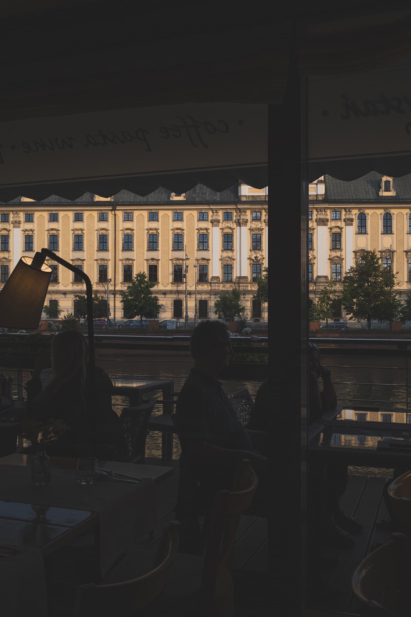 Przystań & Marina — diners silhouetted against golden hour view of Wrocław University across the Oder river